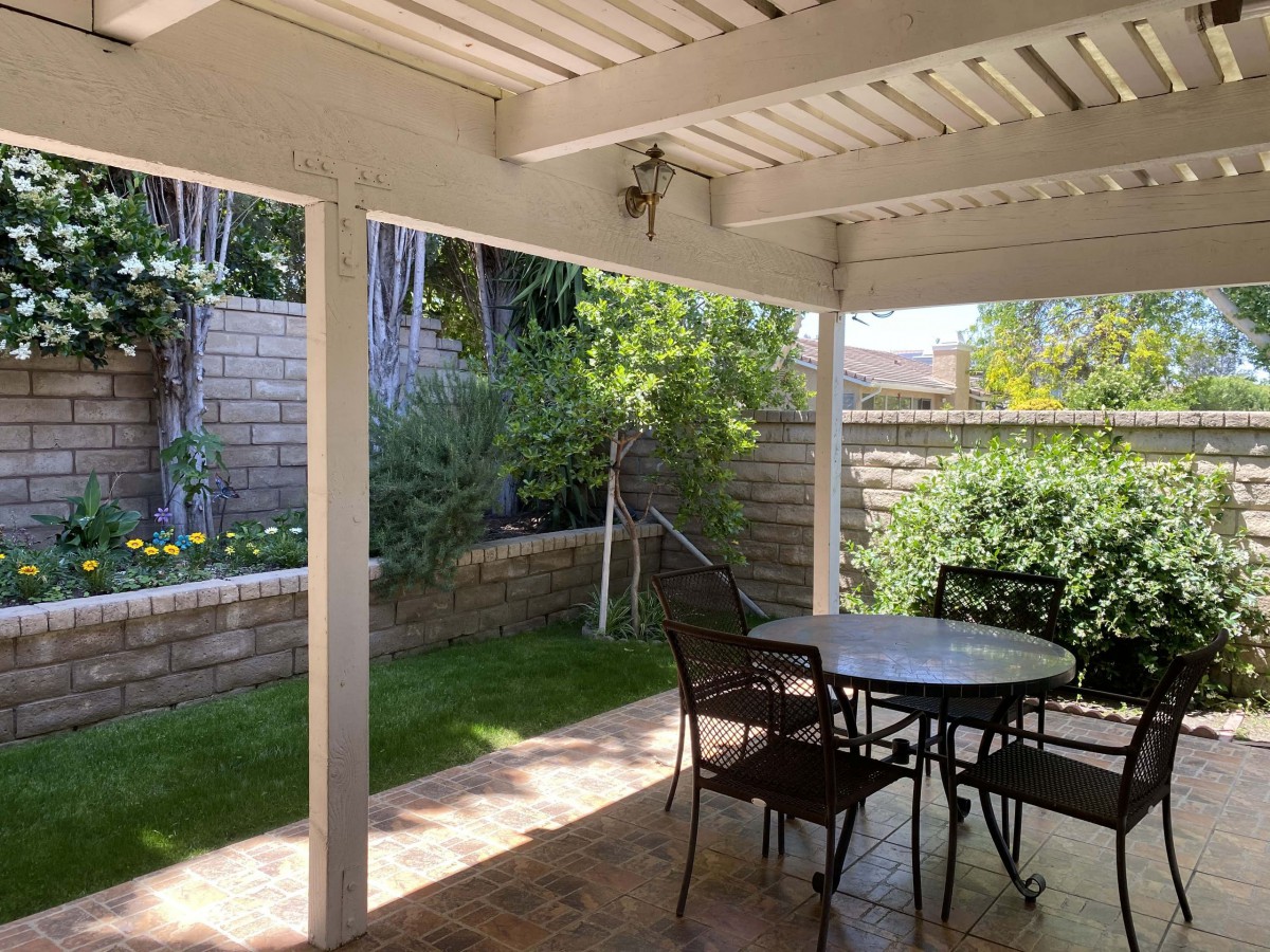 A serene patio with outdoor furniture, surrounded by a lush garden and a brick wall.