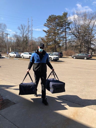 A delivery person carrying two large bags on a sunny day.