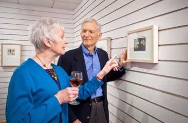 An older couple enjoying a conversation while viewing art at a gallery, with one holding a glass of wine.