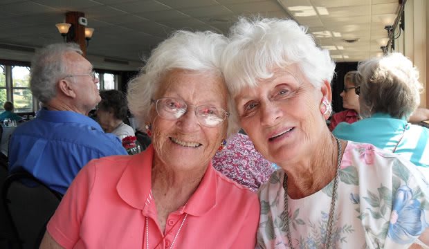 Two elderly women smiling and posing for a photo indoors.