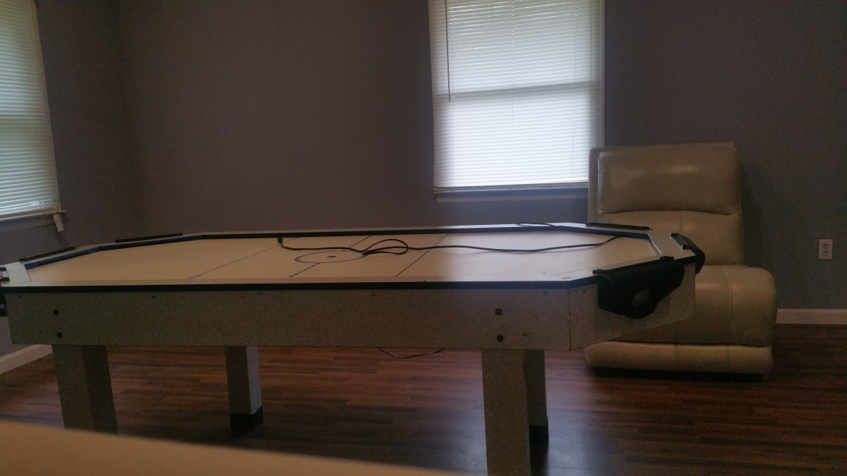 An indoor air hockey table in a recreation room with a window and seating nearby.