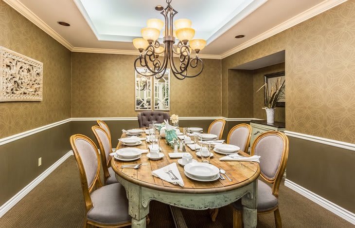 An elegantly decorated dining room with a wooden table set for a meal, highlighted by a chandelier overhead.
