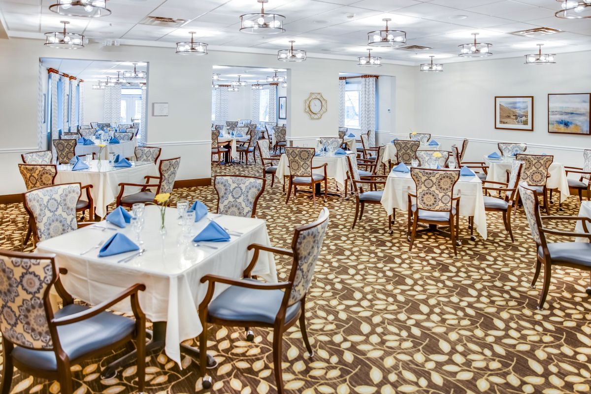 An elegant dining room with neatly arranged tables and chairs, featuring white tablecloths and blue napkins.