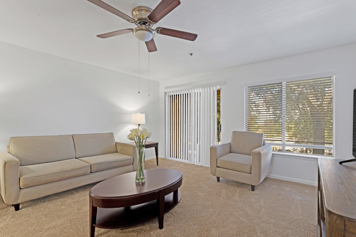 A cozy living room with beige furniture and a ceiling fan.