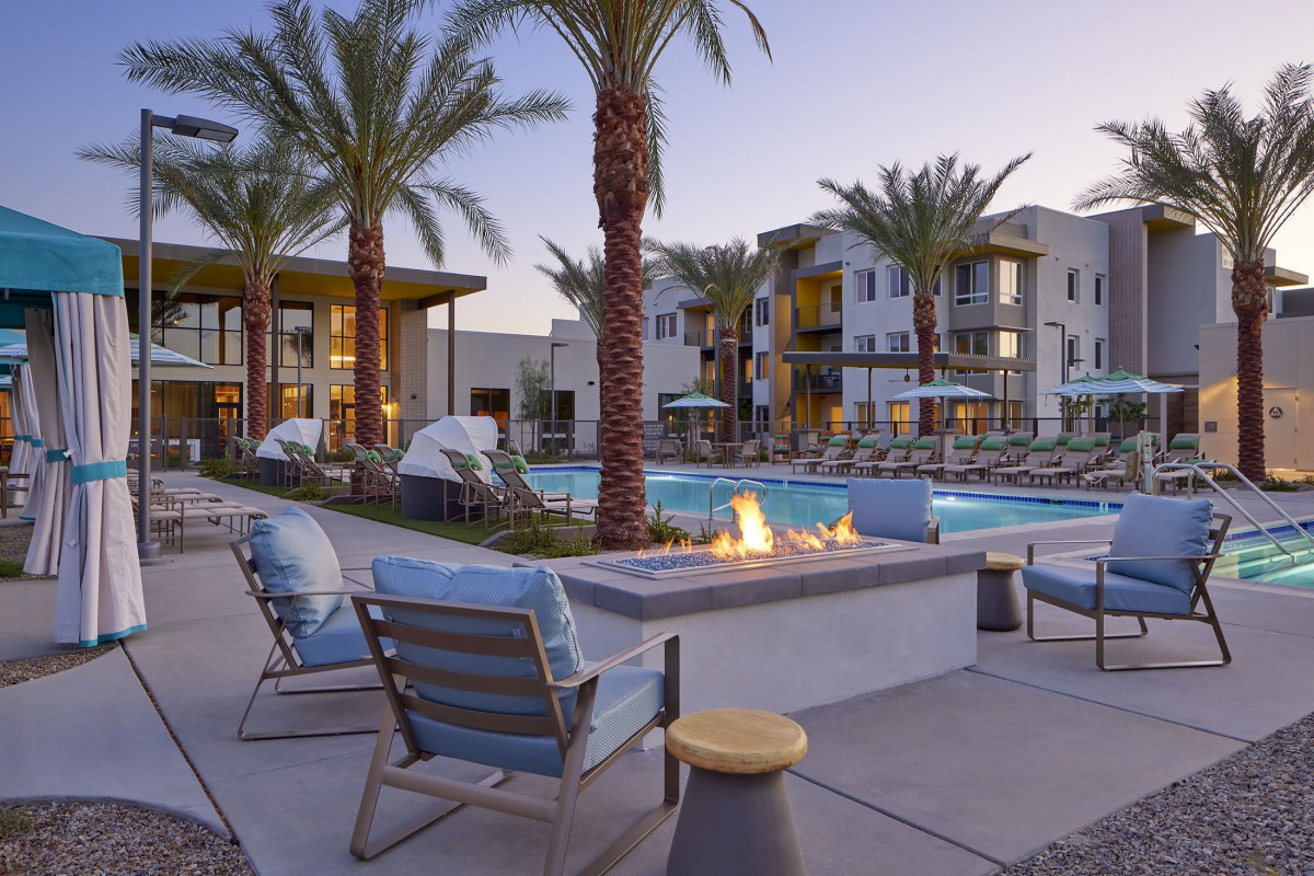 A modern outdoor retreat featuring a pool, fire pit, and lounge area surrounded by palm trees at sunset.
