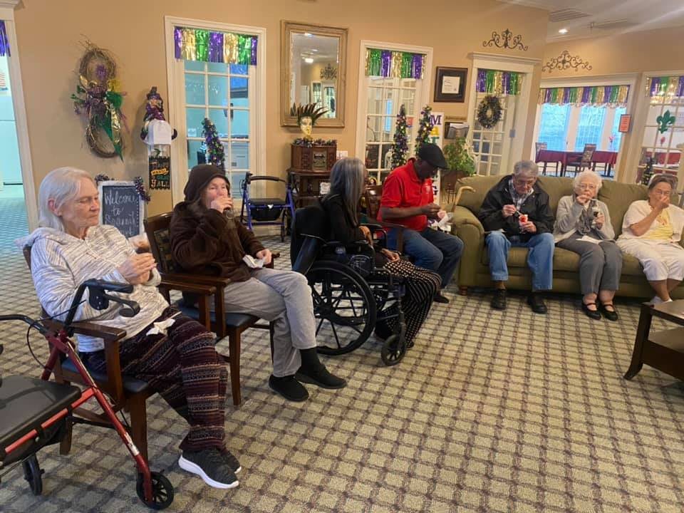 A group of seniors sitting together indoors, some in wheelchairs, enjoying each other's company.