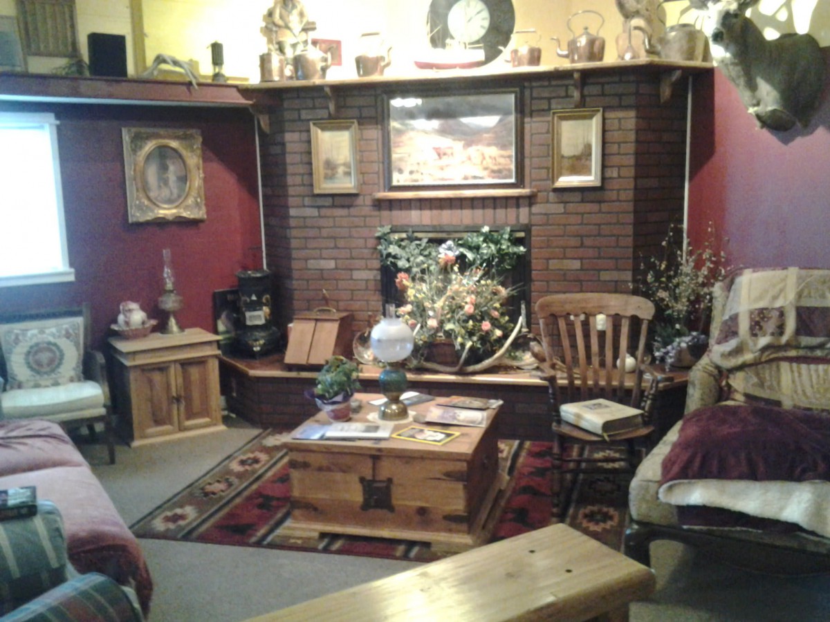 A cozy living room with rustic decor, featuring a fireplace surrounded by wooden furniture and various artworks.