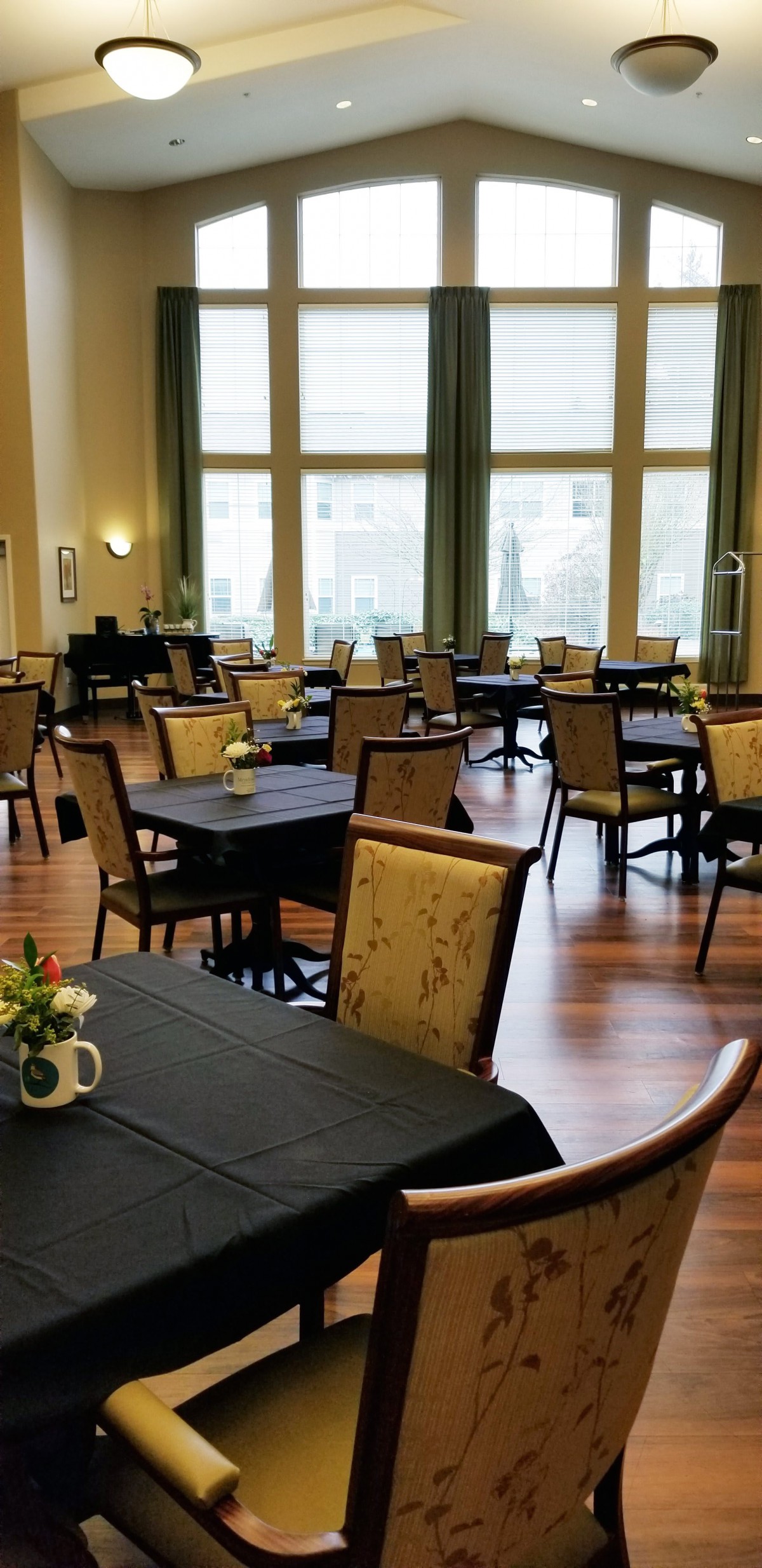 An empty dining room with neatly arranged tables and chairs, featuring large windows and a wooden floor.
