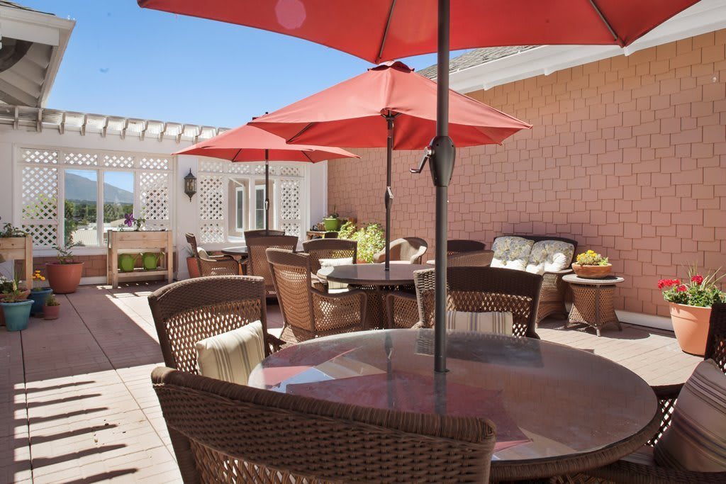 An inviting patio with wicker furniture and bright red umbrellas on a sunny day.