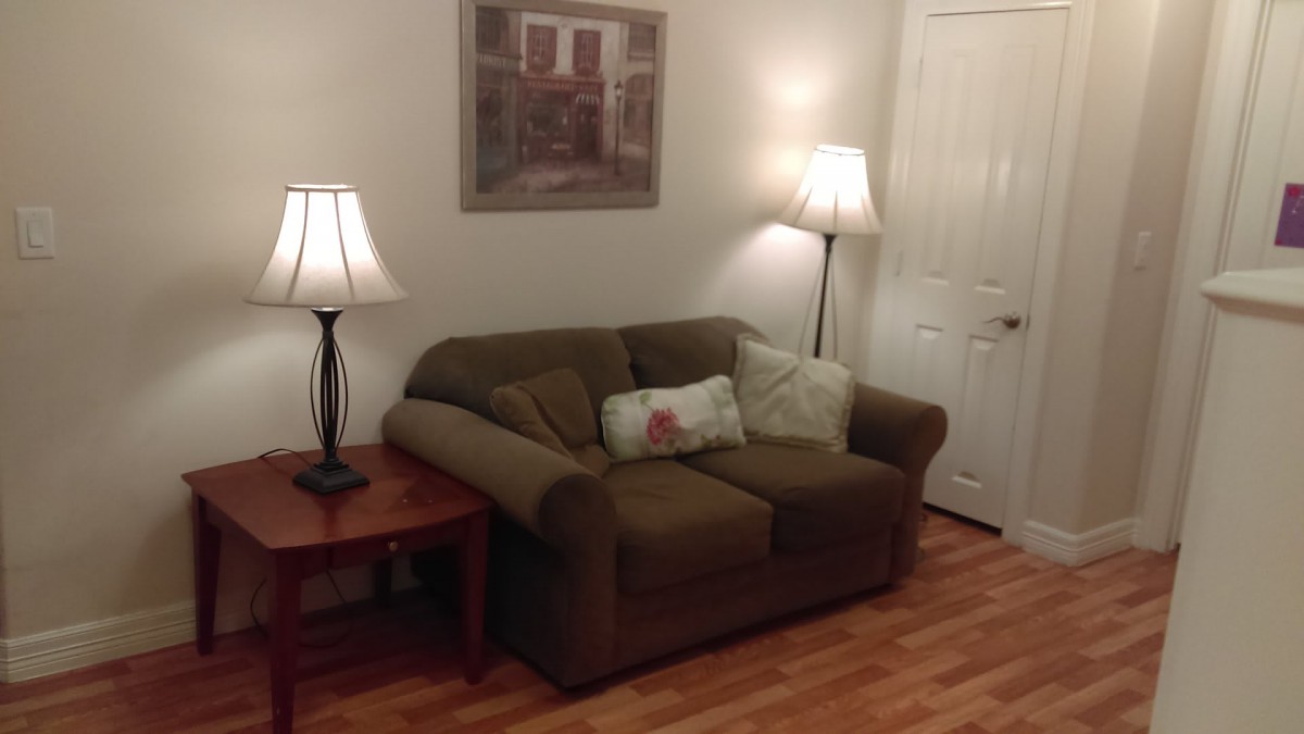 A cozy living room with a brown sofa, two standing lamps, and a painting on the wall.