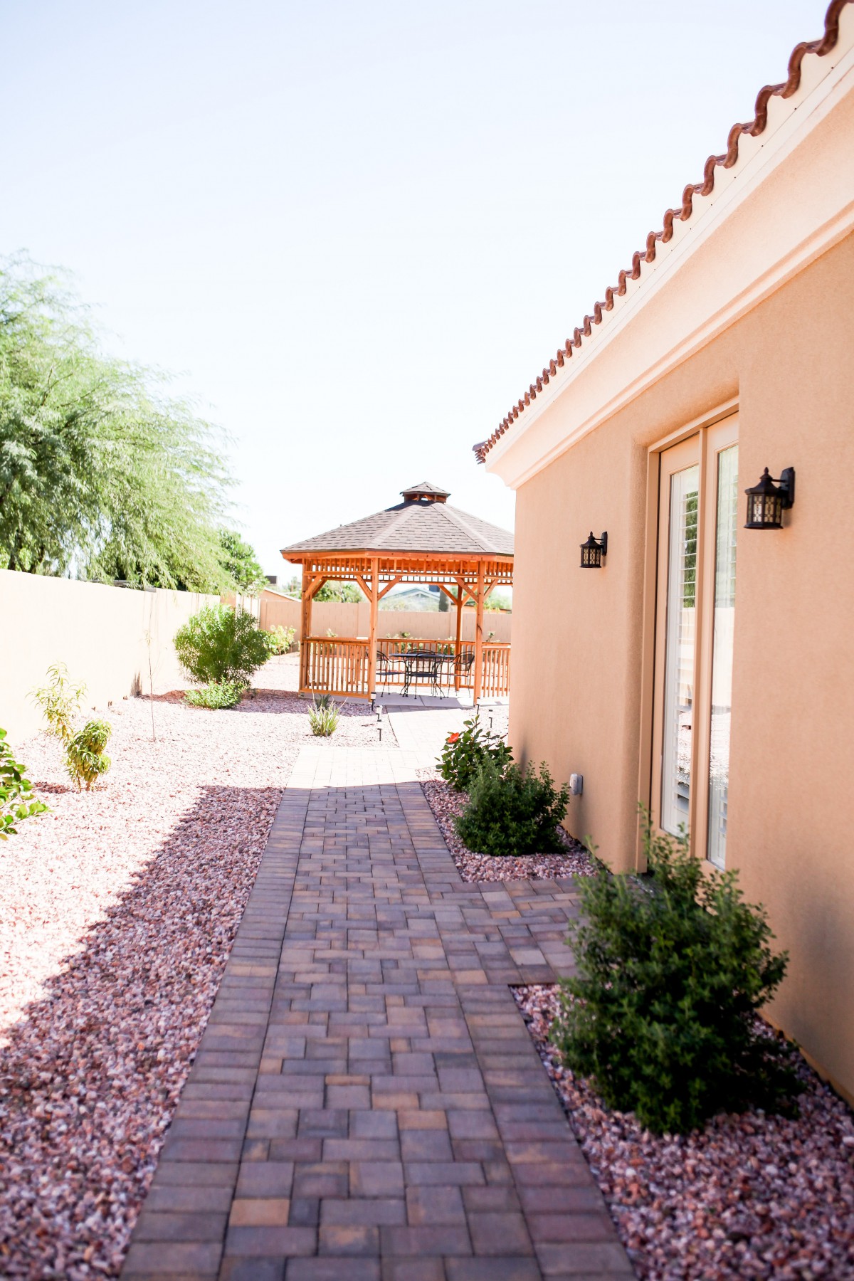 A backyard with a paved walkway leading to a gazebo, surrounded by desert landscaping.