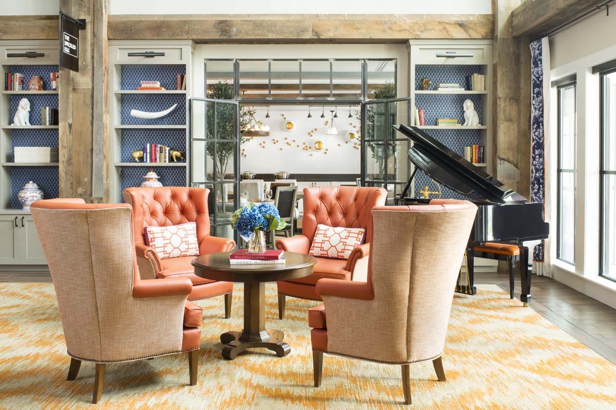 A cozy living room with elegant chairs and a grand piano, surrounded by bookshelves.