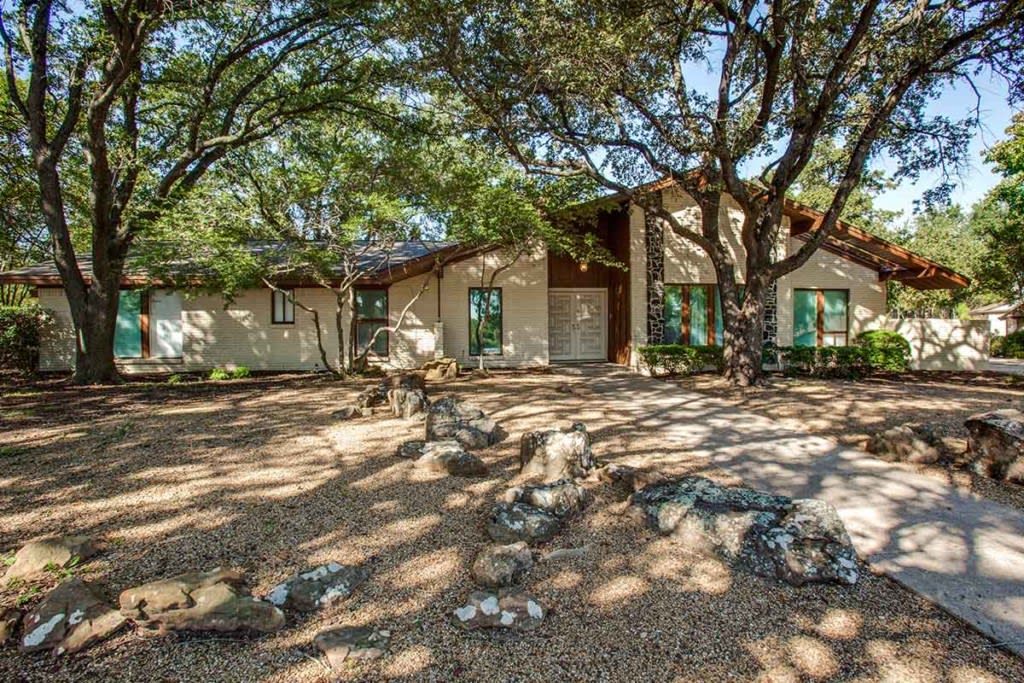 A stone house surrounded by trees with a rustic front yard.