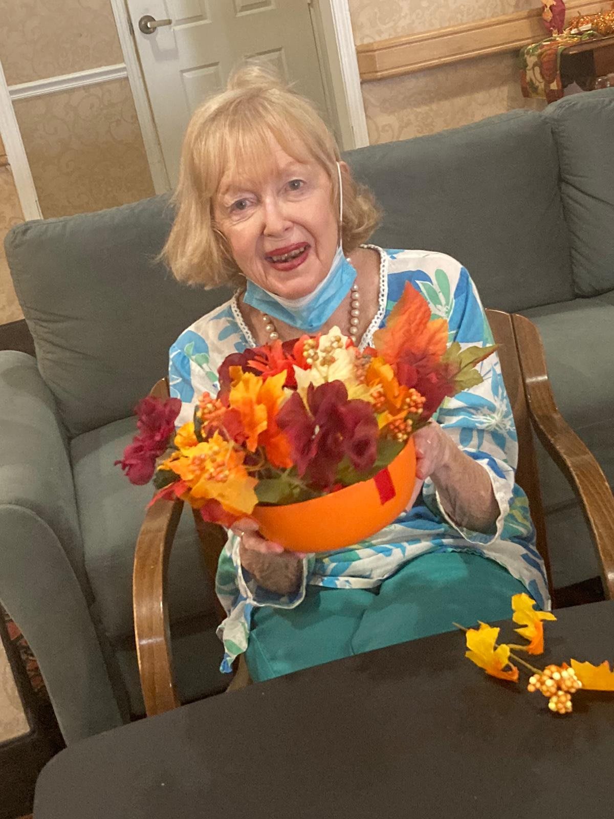 A woman smiling while holding a colorful flower arrangement indoors.