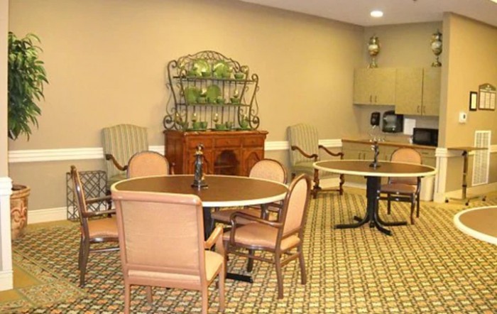 A cozy dining area with round tables and padded chairs, featuring a patterned carpet and decorative shelving.