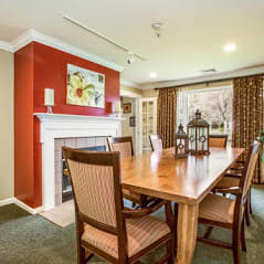 A cozy dining room featuring a wooden table surrounded by chairs, accented with a fireplace and decorative artwork.