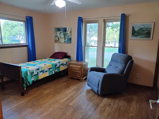 A cozy bedroom featuring a bed, recliner, and large windows allowing natural light.