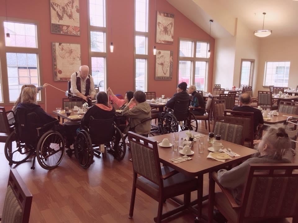 A group of elderly individuals gathered in a dining area, some in wheelchairs, enjoying a meal together.