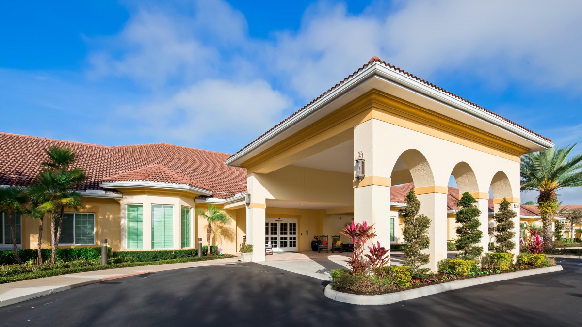 A bright and welcoming building entrance with landscaped surroundings under a blue sky.