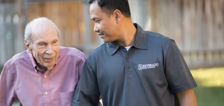 A caregiver providing support to an elderly person outdoors.