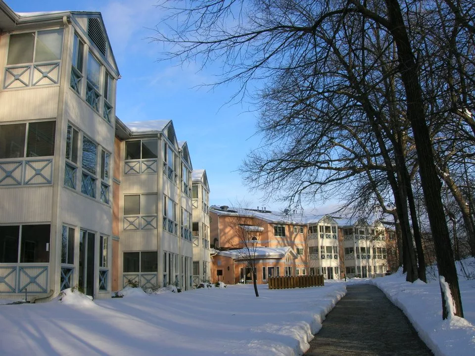 A snowy courtyard between residential apartment buildings under a clear blue sky.