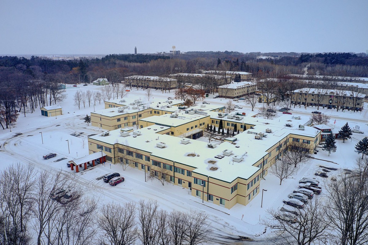 Aerial view of snow-covered buildings surrounded by trees in a winter landscape.