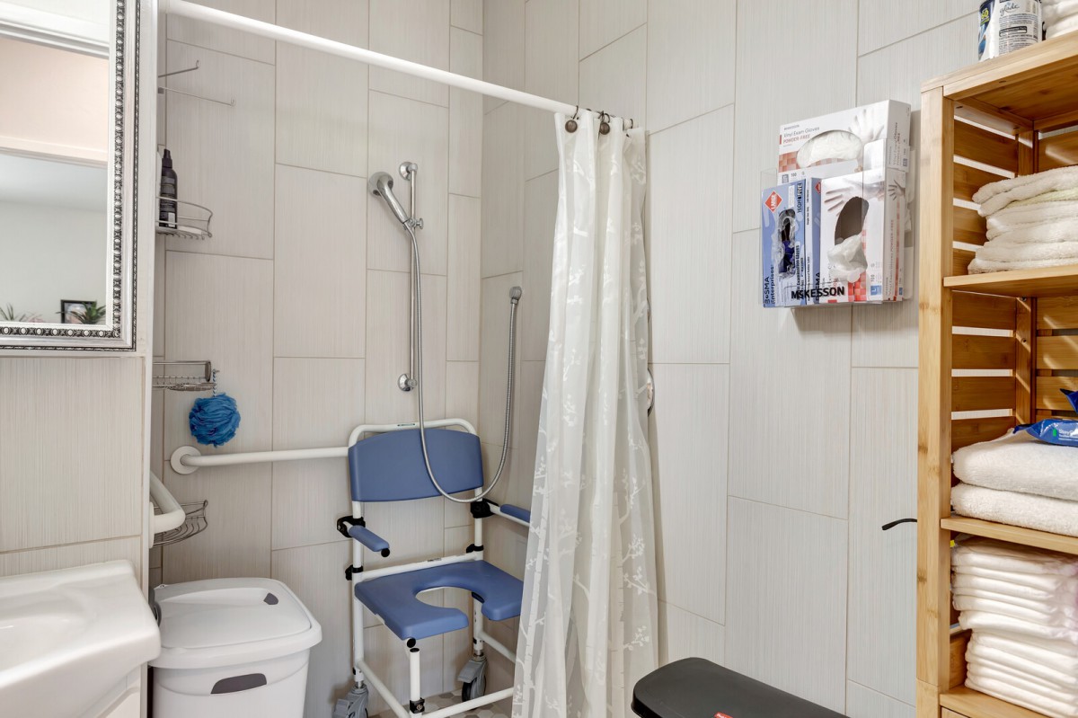 An accessible bathroom equipped with a shower chair, grab bars, and a curtain.