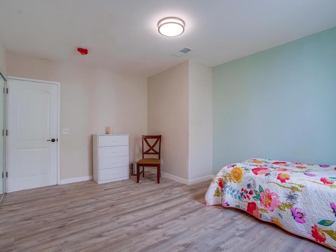 A minimalist bedroom with a single bed, chair, and dresser on wood flooring.