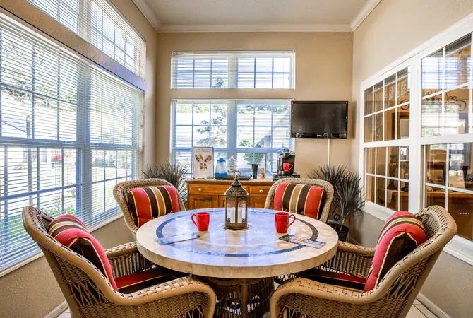 A cozy dining area with a round table and wicker chairs set near large windows, allowing natural light to brighten the space.