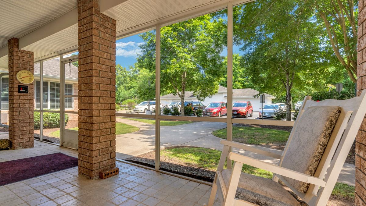 A sunny screened porch overlooking a driveway and lush green trees.