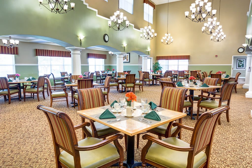 An elegant dining room with neatly arranged tables and chairs under ornate chandeliers.