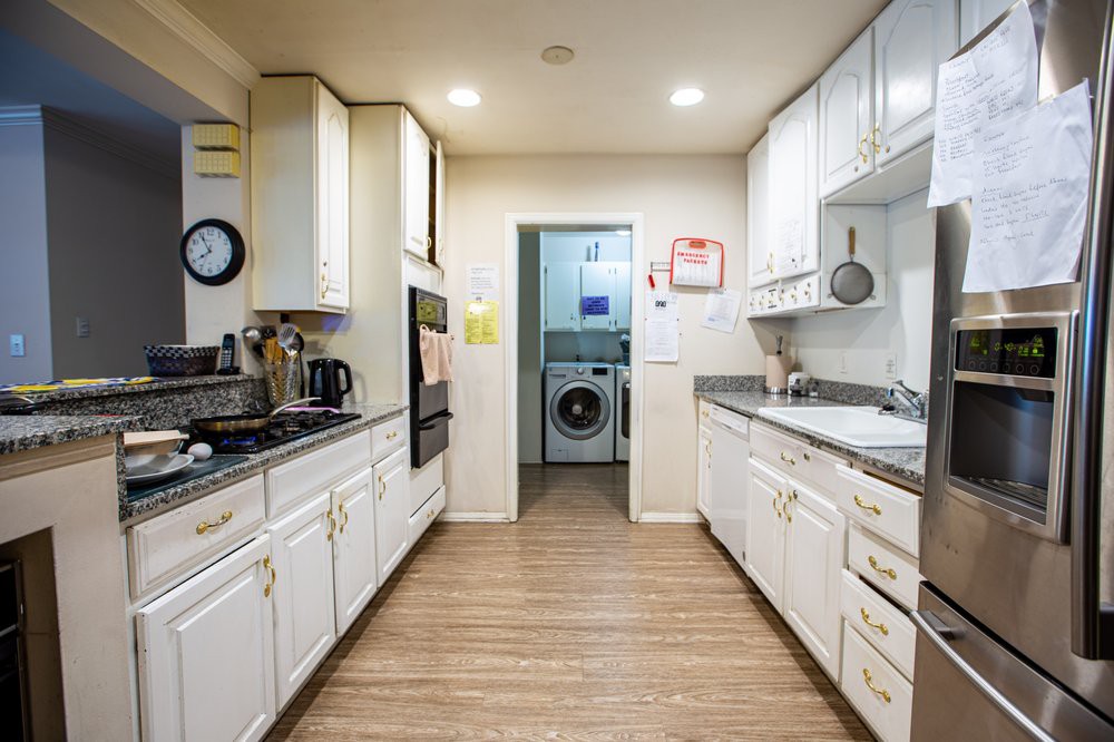 A modern kitchen with white cabinets and wood flooring, leading to a laundry room.