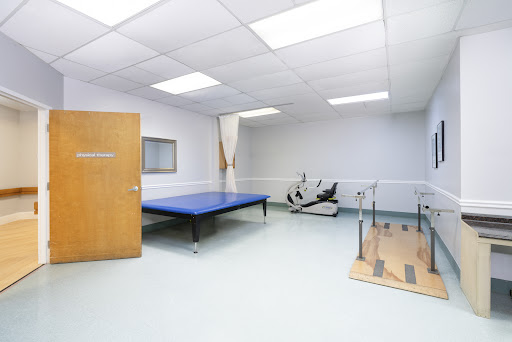A clean and well-equipped therapy room with a blue exercise mat and physical therapy apparatus.
