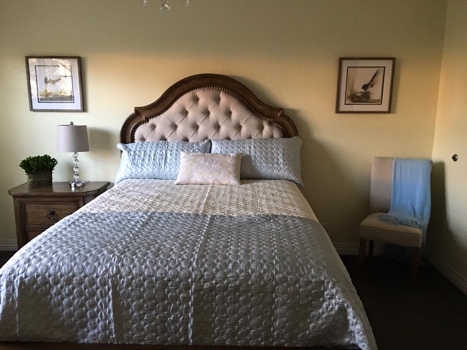 A cozy bedroom with a large bed featuring a tufted headboard, flanked by two side tables and decorated with framed wall art.