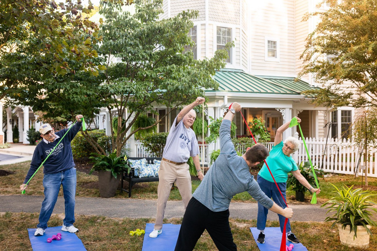 A group of people participating in an outdoor exercise session, performing stretching exercises on yoga mats in a garden setting.