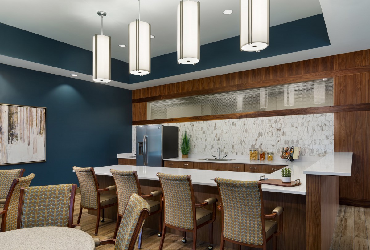 A modern kitchen interior with bar seating, contemporary lighting fixtures, and a marble backsplash.
