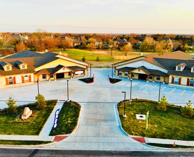An aerial view of a suburban area with buildings, parking lots, and surrounding greenery.