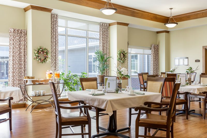 A bright and airy dining room with neatly arranged tables and chairs, adorned with plants and decorative elements.