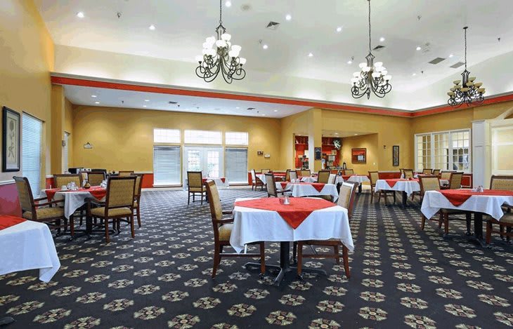 A spacious dining area with neatly arranged tables, elegant chandeliers, and bright lighting.