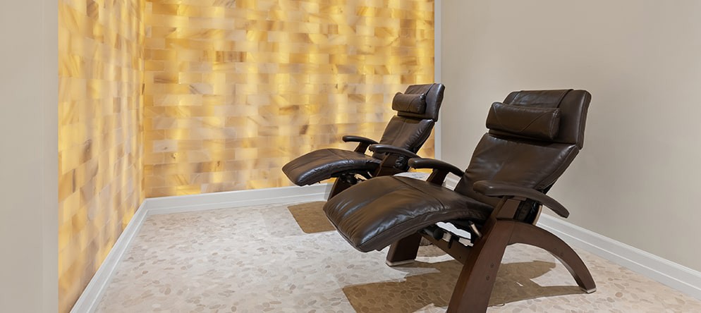 A tranquil therapy room featuring relaxing recliner chairs facing a glowing salt wall.