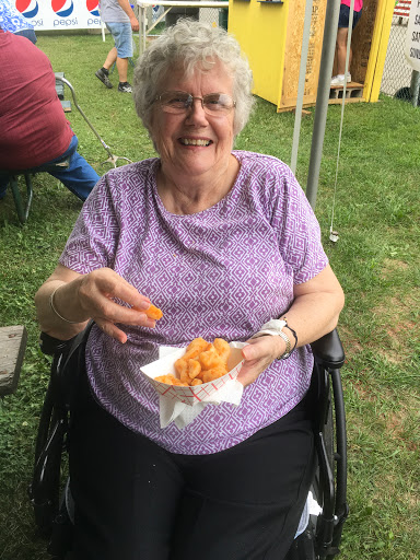 An elderly woman enjoying a snack while seated in her wheelchair at an outdoor event.