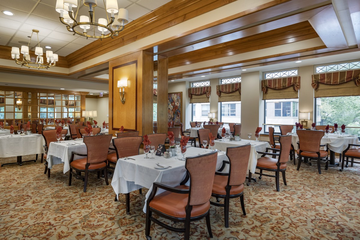 An elegant dining room with neatly arranged tables and chairs, featuring chandeliers and a carpeted floor.