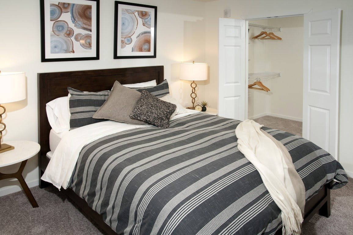 A modern bedroom with striped bedding, framed artwork, and an open closet.