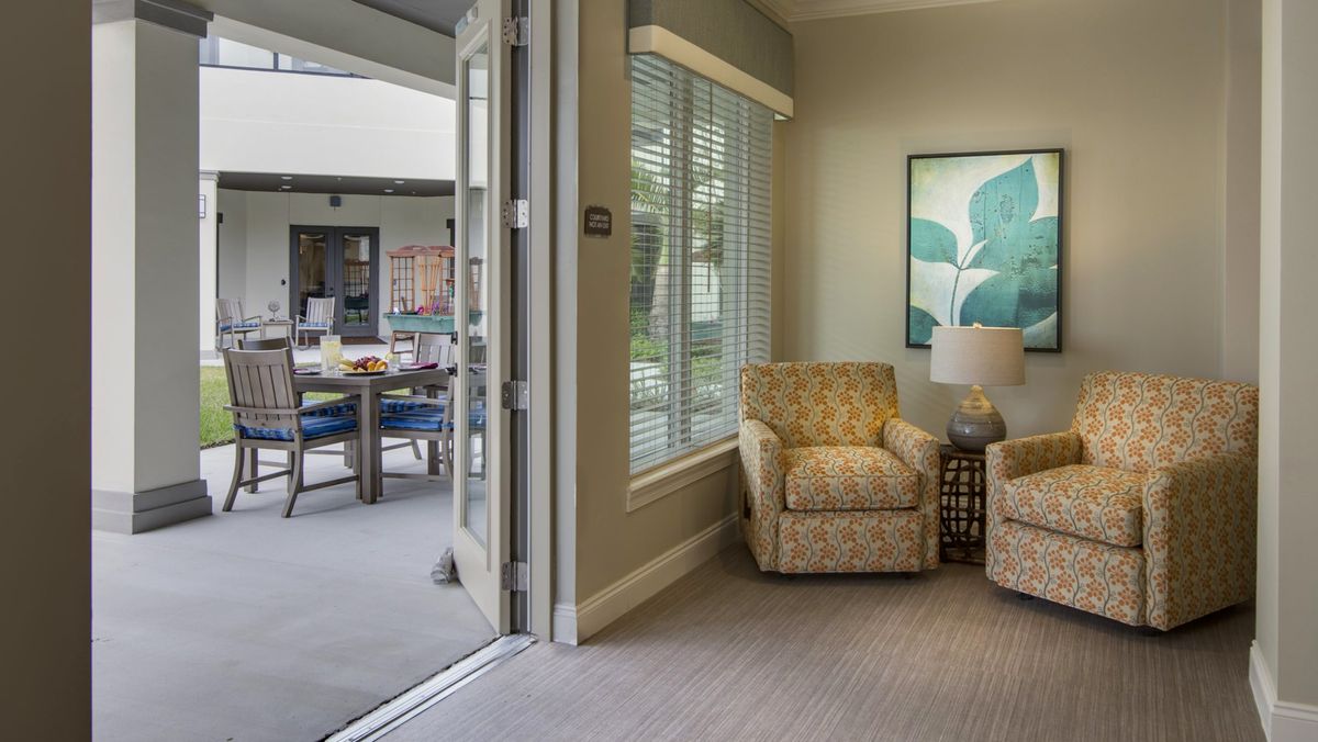 A cozy living room with an armchair and a lamp near a window, opening to a patio.