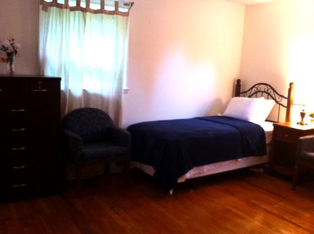 A cozy bedroom with a single bed, chair, and dresser on a wooden floor.