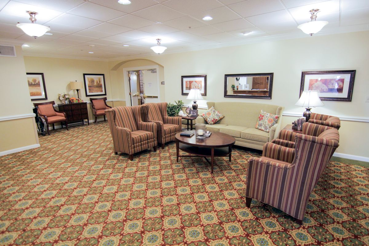 A cozy living room with a sofa, armchairs, and a coffee table set on a patterned carpet under ceiling lights.