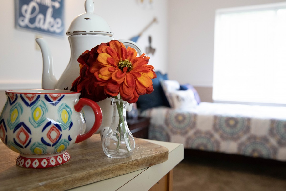 A cozy bedroom corner with a vase of vibrant flowers, colorful teapot, and cup.