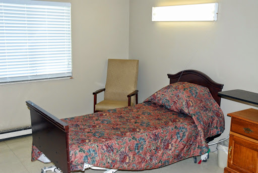 A simple and tidy bedroom featuring a bed with patterned bedding, a chair, and a window.