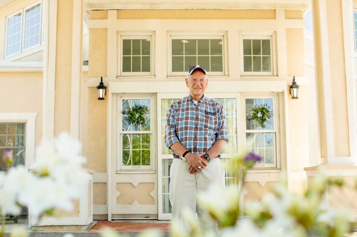 A person stands in front of a building surrounded by flowers.