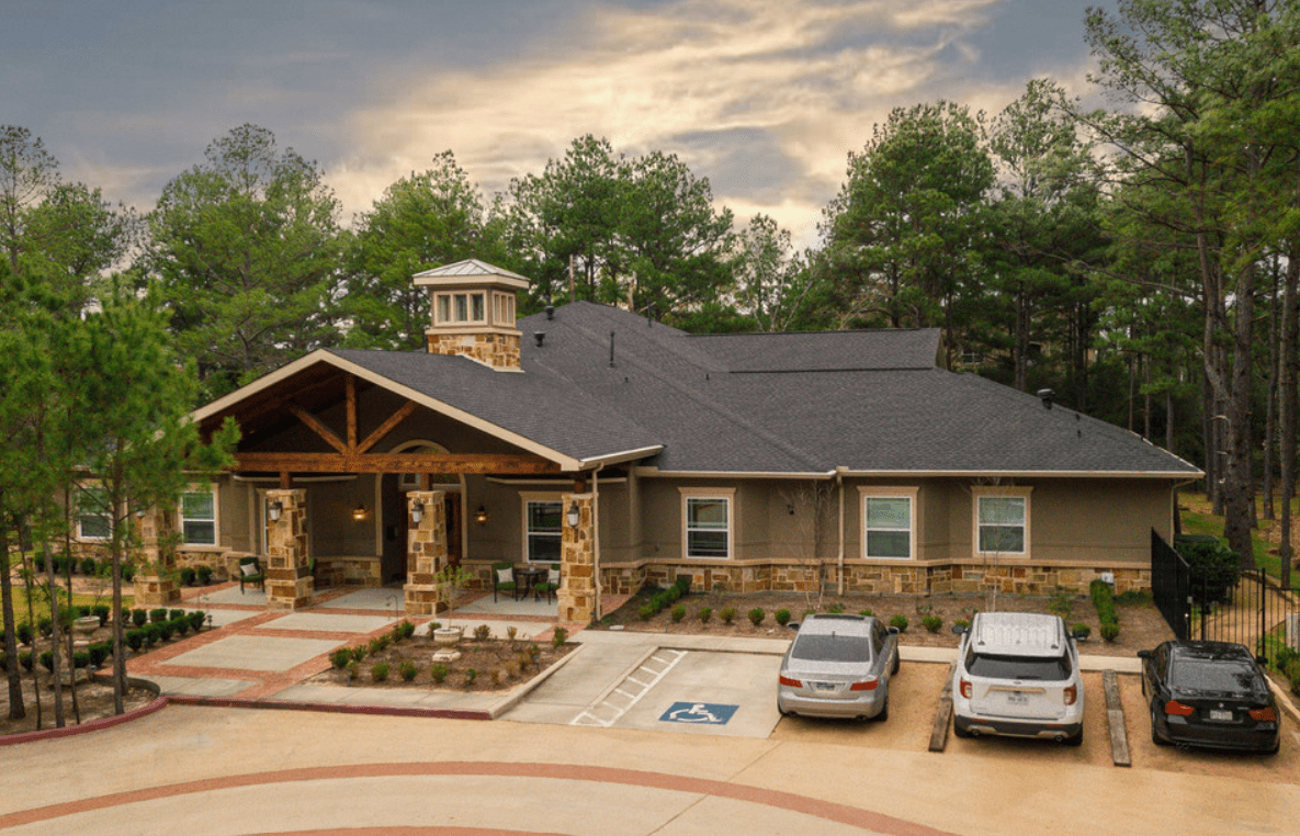 A picturesque house with a parking lot, surrounded by trees under a cloudy sky.